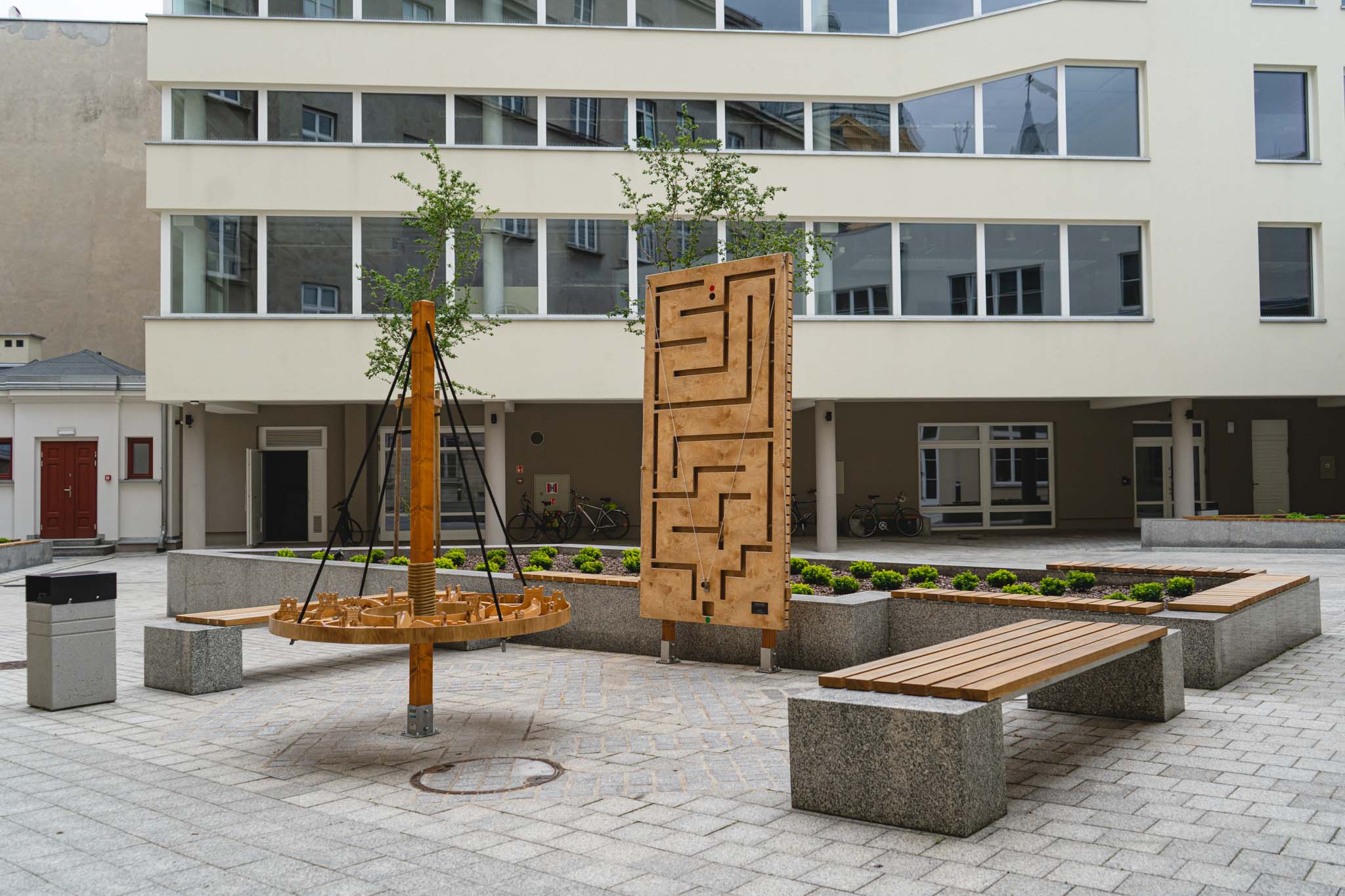 Elewacja budynku Muzeum Archeologicznego i Etnograficznego w Łodzi wraz z dziedzińcem, na którym stoją ławki oraz atrakcje dla dzieci.