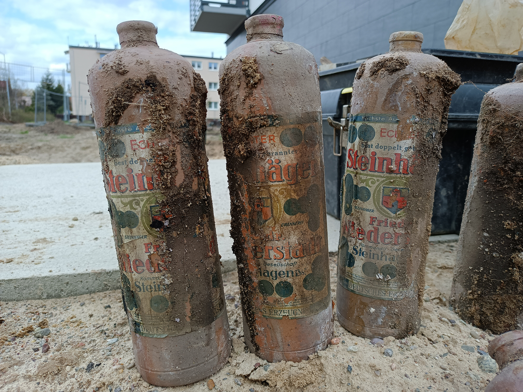 Trzy stojące butelki z etykietami oblepione ziemią