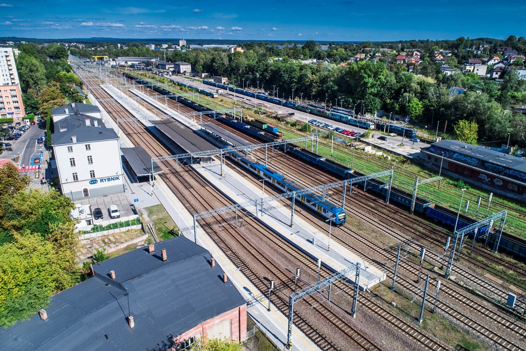Widok z lotu ptaka na tory kolejowe, budynek stacji Rybnik, dachy peronów, pociąg